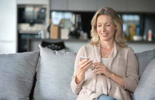 A Middle age woman sitting on a grey sofa looking at her phone