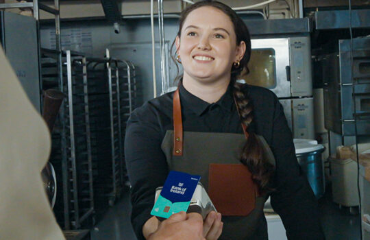 A woman holding a card machine while another person taps their Bank of Ireland business debit card.