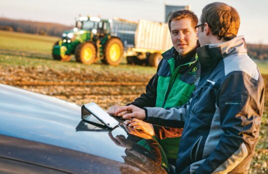 Two man having a discusion in a field with a tractor behind