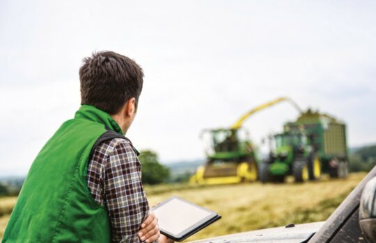 A farmer with a tablet in the hands looking at two tractors